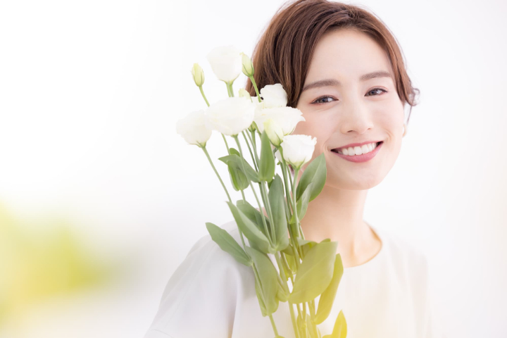 セラミックの美しい歯に満足して微笑む花を手にした女性